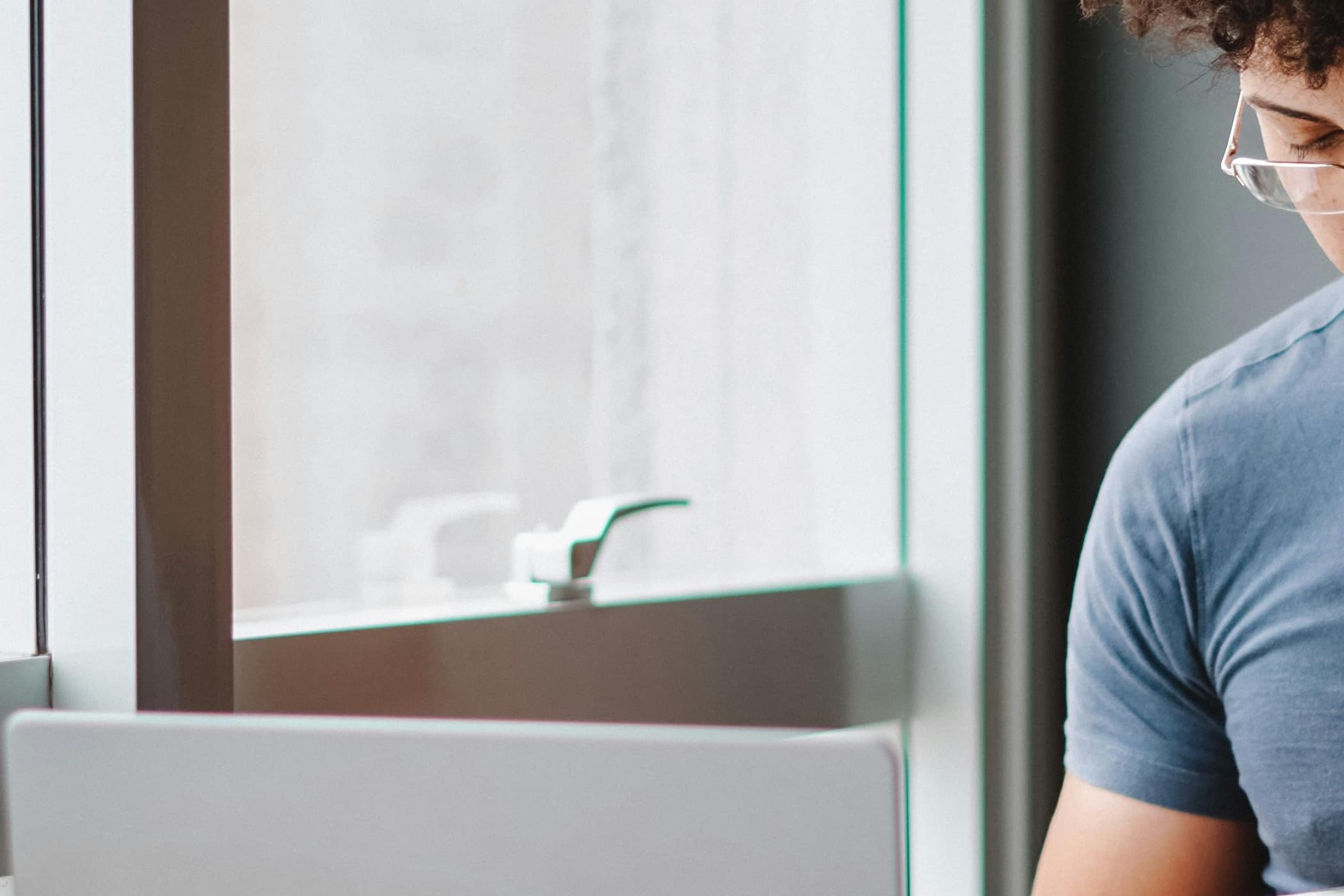Young man checking his phone beside a laptop in a bright cafe workspace